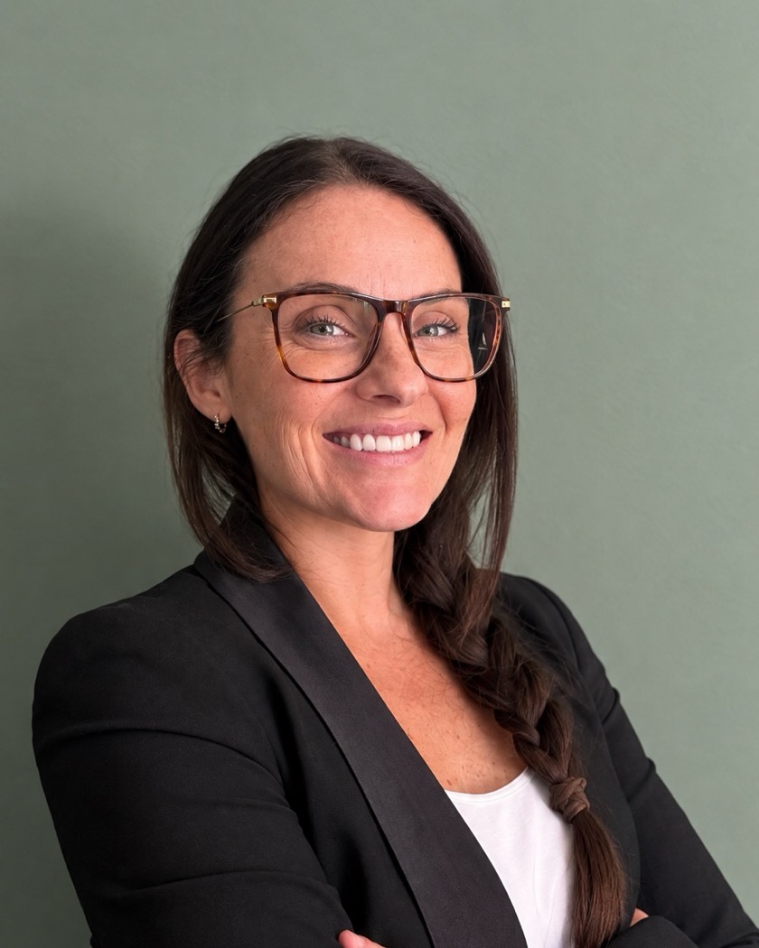 Cristiana Cantomelo, smiling, in a black blazer against a sage-green wall